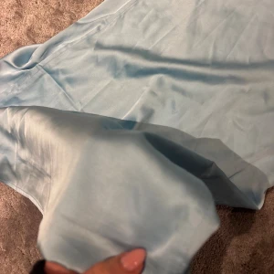 Ljusblå långkjol från Edikted - Supersnygg ljusblå långkjol från Edikted i glansigt satintyg. Kjolen har en enkel och stilren design med rak passform samt en spets och rosett detalj längt toppen. 