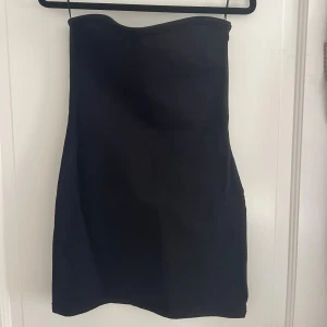 Svart bandue klänning från Zara - Säljer en svart, axelbandslös kort klänning från Zara i storlek XS. Materialet är något grövre så lägger sig finare mot kroppen. Passar en S men kan bli något kort om du är lång!