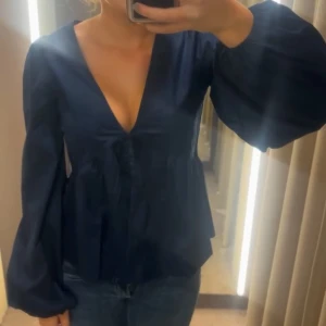 Svart blus med ballongärmar och v-ringning - Säljer en marinblå blus från Nelly. Helt ny och säljs inte längre. Köpt för 499 kr.