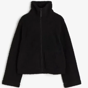 Svart teddyjacka med dragkedja - Mysig svart teddyjacka med hög krage och hel dragkedja framtill. Jackan har två stora fickor och en rak, något boxig passform. Perfekt för kyliga dagar när du vill vara både varm och stilren.