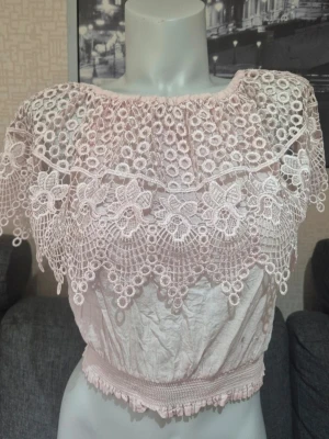 Ljusrosa spetsig bolerotopp - Supersöt ljusrosa bolerotopp med bred, detaljerad spets och broderade blommor. Toppen är croppad och har elastisk midja för skön passform. Perfekt för dig som vill ha en romantisk och unik look med offshoulder-stil.Storlek XS, S/M 🌸🩷 ingen storleksetikett 🛍