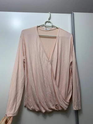 Ljusrosa omlottopp från Cubus - Säljer en ljusrosa omlottopp från Cubus i storlek XS. Toppen har lång ärm, djup v-ringning och omlottdetalj framtill som ger en snygg draperad effekt. Materialet är mjukt och tunt, perfekt för vår och sommar. Passar även S.