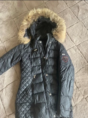 Svart lång dunjacka med pälsluva - Säljer en jättefin svart jacka från Rockandblue med flera praktiska detaljer. Jackan har en stor huva med fluffig päls, dragkedjor och knappar framtill samt flera fickor med dragkedja. Jackan sitter precis under rumpan på mig som är 169cm. (Aldrig använd!) kontakta privat vid intresse!💖