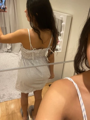 Randig sommarklänning med smock - Superfin kort klänning med smala axelband och smock upptill. Ljusblå och vit randigt mönster, perfekt för varma dagar. Klänningen har en luftig passform och är tillverkad i ett mjukt bomullstyg. Söt och enkel att styla med sneakers eller sandaler.