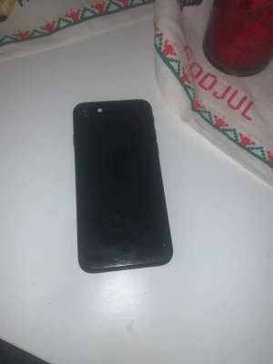 iPhone SE  - Svart iPhone SE med synliga repor och fingeravtryck på baksidan. Telefonen är igång och visar inställningsskärmen, vilket indikerar att den fungerar. Mindre kosmetiskt slitage, men i övrigt ser den ut att vara i bra skick.  128gb 