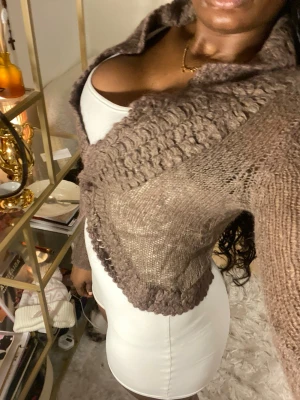 Brun stickad kofta med grov krage - Säljer en brun, kort stickad kofta med grovstickad krage och kant. Koftan har lång ärm och är i ett mjukt, fluffigt material som känns riktigt mysigt. Perfekt att slänga över en topp för en chill look.