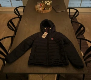Blå Fjällräven Expedition dunjacka M - Säljer en blå Fjällräven Expedition Series dunjacka med huva och gul snörning. Jackan har klassisk Fjällräven-logga på bröstet, quiltad design och dragkedja framtill. Den är helt ny men prislapp på. Säljer då den inte passar mig!