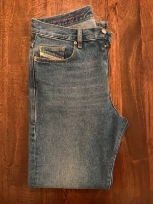 Blå Diesel 2020 jeans straight fit - Säljer ett par klassiska blå jeans från Diesel, modell 2020 5 Pocket. De har rak passform, midwaist och fem fickor. Jeansen är tillverkade i slitstark denim och har subtila detaljer som Diesel-logga på fickan. Perfekt för dig som gillar tidlös stil.