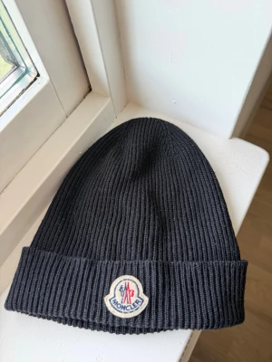 Svart Moncler mössa  - Svart ribbstickad mössa från Moncler med loggan framtill. Äkta från CareofCarl originalpris 2499kr. Kom med prisförslag :)