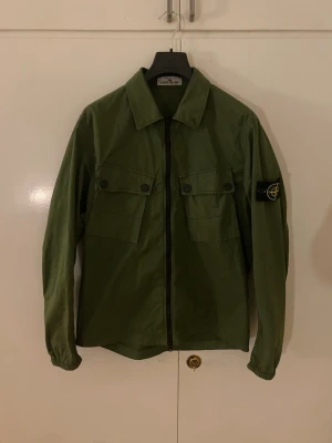 Grön overshirt från Stone Island - En riktigt snygg overshirt från Stone Island. Köpt på NK Stockholm, kvitto och tagg tillkommer! Nypris ca 4500kr. Storlek M. Super fint skick! Hör av er vid eventuella frågor.