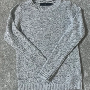 Grå stickad tröja med paljetter - Snygg grå stickad tröja med diskreta paljettdetaljer som ger lite extra glans. Rund halsringning och långa ärmar med ribbade muddar. Perfekt för dig som gillar enkel stil med en twist.❤️