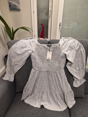 Bik Bok DW Air grå klänning storlek M - Supersöt ljusgrå klänning från Bik Bok med smockad överdel och volangkjol. Klänningen har långa ärmar med broderade detaljer och elastiska muddar. Materialet känns mjukt och luftigt, perfekt för vår och sommar. Säljes med etikett kvar.