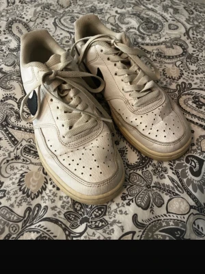 Nike skor  - Nike sneakers i vitt skinn med svart swoosh på sidan. Klassisk rund tå, snörning och platt sula. Perforerade detaljer på tån för extra ventilation. Har creasat och är smutsiga där utav priset. Köpt för 799