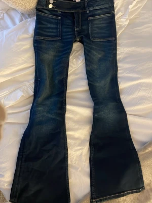 Blå low waist, bootcut jeans från Gina Tricot - Snygga blå jeans med bootcut från Gina Tricot. Modellen är låg midjade, stora fickor fram och klassiska bakfickor. Jeansen är i denim med slitningar och har silverfärgade knappar samt dragkedja. Perfekt för dig som gillar retrovibbar och markerad siluett.💙 