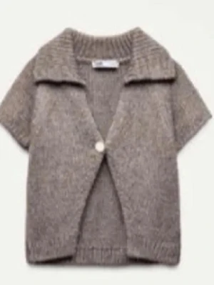 Beige stickad kofta med krage - Kortärmad beige stickad kofta med bred krage och en knapp framtill. Koftan har ribbade detaljer vid krage, ärmslut och nederkant, vilket ger en snygg och avslappnad look. Perfekt att slänga över en t-shirt för extra stil.