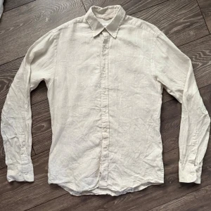 Beige linneskjorta från John Henric - Snygg beige skjorta från John Henric i 100% linne. Klassisk krage, långärmad och med knappar hela vägen framtill. Perfekt för dig som gillar en clean och chill stil. Skjortan har en avslappnad passform och är designad i Sverige.