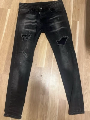 Svarta skinny jeans från Dsquared2 - Svarta jeans från Dsquared2 i storlek 48 med skinny passform. Snygga slitningar och hål på benen ger en cool, edgy vibe. Jeansen har klassisk femficksdesign och är tillverkade i jeansmaterial med lite stretch för extra komfort.