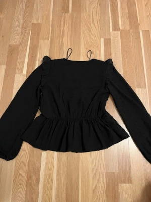 Svart blus - En svart blus som har andvänds ett fåtal gånger och är perfekt om man vill vara lite fin. Blusen är v ringad med volanger runt och vid axlarna.