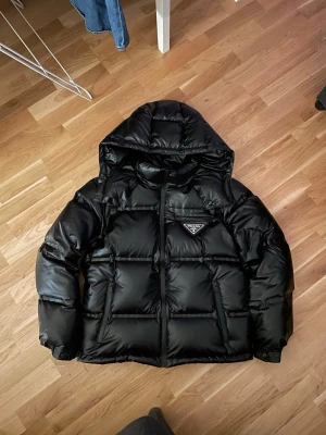 Svart prada jacka  - Säljer min svarta Prada jacka, kvalitet 9/10✨. Fin svart färg med stor loga. Haft jackan ett litet tag och inga spår av defekter. Storlek: L, sitter perfekt mot kroppen och har ej ”baggy form”. Perfekt vinter jacka med stil. Vid fler frågor, skicka iväg ett pm!