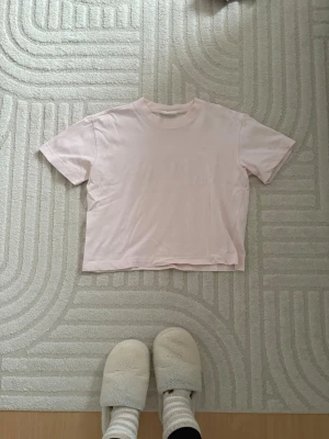 Ljusrosa t-shirt från Gina Tricot - Säljer en ljusrosa t-shirt från Gina Tricot, basically basics-kollektionen. Modellen är kortärmad med rund hals och har en clean, enkel look. Materialet är mjuk bomull som känns skönt mot huden. Perfekt för dig som gillar minimalistisk stil.