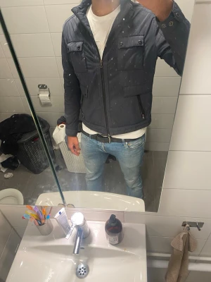 Mörkblå quiltad vindjacka med dragkedja - Snygg mörkblå vindjacka med quiltad design och hög krage. Jackan har två bröstfickor med knappar, två sidofickor med dragkedja och knappdetaljer vid ärmslut. Perfekt för dig som gillar stilren och sportig look.