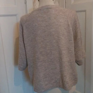 Beige stickad tröja från 157, S - Mysig beige stickad tröja från 157 med rund halsringning och trekvartsärm. Tröjan har en avslappnad passform och ribbade muddar vid ärmslut och nederkant. Perfekt för lager på lager under kyliga dagar.