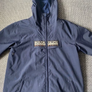 Napijri windbreaker  - Snygg mörkblå vindjacka från Napapijri. Jackan har tydlig logga på bröstet och en patch på ärmen. Tillverkad i polyester och har två fickor med dragkedja. Perfekt för matchdagar och streetwear-stil. Pris kan diskuteras 