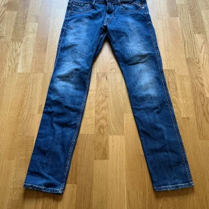 Replay Anbass blå jeans herr - Snygga blå Replay Anbass jeans med klassisk femficksdesign och diskreta slitningar. Jeansen har normal passform och raka ben, med detaljerade sömmar på bakfickorna. Tillverkade i mjukt denimtyg för en bekväm känsla. W32/L30
