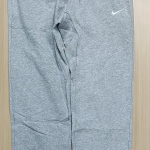 Grå mjukisbyxor från Nike, storlek M - Grå mjukisbyxor från Nike med klassisk vit swoosh-logga på höften. Byxorna har en avslappnad passform och är tillverkade i mjukt bomullsmaterial, perfekta för chill dagar eller träning. Elastisk midja och sidofickor för extra komfort.