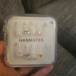 Dekorativa lösnaglar med stenar - Säljer ett set med genomskinliga lösnaglar i storlek M från HANMATES. Naglarna är dekorerade med glittrande stenar och holografiska detaljer för en extra snygg look. Perfekt för dig som vill ha unika och trendiga naglar utan att gå till salong.
