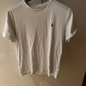 Vit t-shirt från Polo Ralph Lauren - Vit t-shirt från Polo Ralph Lauren med klassisk broderad logga på bröstet. T-shirten har rund halsringning och korta ärmar, tillverkad i mjuk bomull. Enkel och stilren design som funkar till allt.
