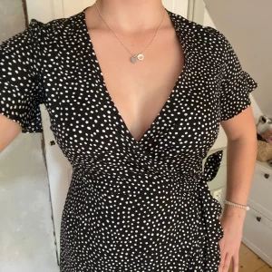 Svart prickig omlottklänning Vero Moda - Supersöt svart omlottklänning med stilren v-ringning och volangdetaljer. Knyts i midjan och ger det en fin passform. Är storlek xs men skulle säga den passar även S och M. Använd fåtalet gånger ⚡️💕