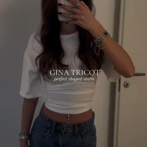 Vit croppad topp från Gina Tricot - Säljer en vit croppad topp från Gina Tricot med korta ärmar och tight passform. Toppen har snygga rynkade detaljer i midjan som ger en cool look. Perfekt att matcha med höga jeans för en trendig stil.