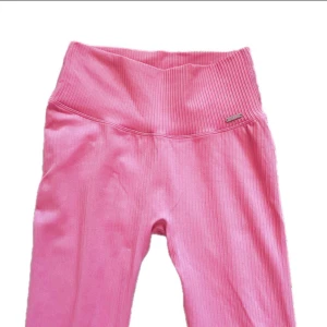 Rosa ribbade leggings med hög midja - Snygga rosa leggings med ribbad struktur och bred, hög midja som sitter skönt. Perfekta för träning eller chill. Stretchigt material som formar sig efter kroppen och ger en tight passform. Liten metallogo på sidan av midjan för extra detalj.