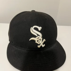 Svart White Sox keps från New Era - Snygg svart keps från New Era 59FIFTY med White Sox-logga broderad i vitt framtill. Klassisk basebollmodell med böjd skärm och MLB-logga baktill. Perfekt för dig som gillar sportig streetstyle och vill ha en ikonisk look. Flitigt använd nypris 500, tveka inte att fråga om det är något ni undrar.                                              MVH