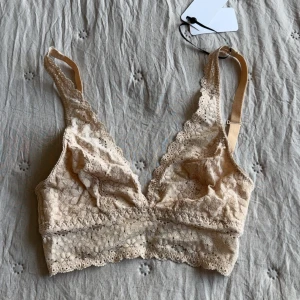 Oanvänd Beige spets bralette från Wacoal - Superfin beige bralette från Wacoal i modellen Halo Lace. Topp i mjuk spets med blommigt mönster, justerbara axelband. Man kan knäppa ihop axelbanden där bak.🫶🏻