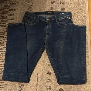 Blå Replay jeans herr, storlek 30 - Snygga blå jeans från Replay i klassisk femficksmodell. Jeansen har raka ben, normal passform och tydliga Replay-detaljer på fickorna. Materialet är slitstarkt denim i bomull och färgen är mörkblå med lätt tvättade partier för en cool look.