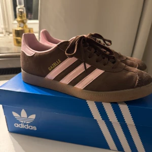 Adidas Gazelle brun/rosa sneakers - Säljer ett par Adidas Gazelle sneakers i brunt mocka med ljusrosa detaljer. Nästan aldrig använda. Nypris: 1245:-