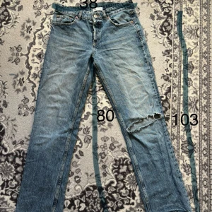 Blå raka jeans från ZARA med hål - Säljer ett par klassiska blå jeans från ZARA med raka ben och ett stort slitet hål på ena knät. Jeansen har fem fickor, knappgylf och coolt tvättad denim-look. Perfekta för dig som gillar en avslappnad och trendig stil.