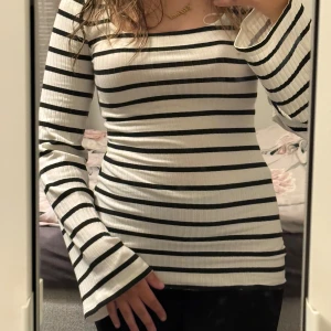 Randig ribbad långärmad topp - Säljer en vit och svart ribbad topp med horisontella ränder. Toppen har lång ärm med lätt utsvängda ärmslut och en fyrkantig ringning. Sitter figurnära och är superenkel att styla till jeans eller kjol.