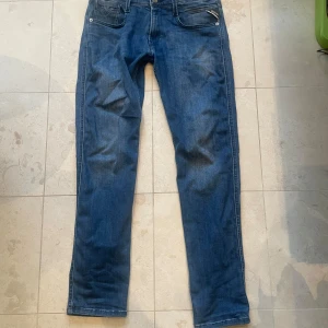 Replay Anbass slim fit jeans blå - Säljer ett par blå Replay Anbass jeans i slim fit. Klassisk femficksmodell med dragkedja fram och snygga detaljer på bakfickorna. Jeansen är i stretchigt denim och har en modern passform som sitter snyggt på benen.