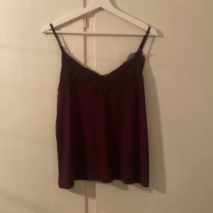 Vinröd linnetopp med spets från Amisu - Säljer en vinröd linnetopp från Amisu med tunna axelband och vacker spetsdetalj längs urringningen. Toppen har en mjuk, flowy passform och är perfekt för dig som gillar en stilren men ändå romantisk look.