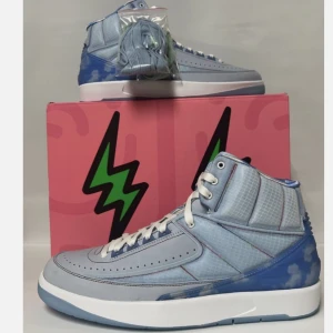 Nike Jordan 2 blå sneakers - Snygga Nike Jordan 2 sneakers i ljusblått med vita och blå detaljer. Skorna har rutmönstrad textil, vita snören och en cool blå häl med molnliknande mönster. Perfekta för dig som vill sticka ut med stilrena och unika sneakers.