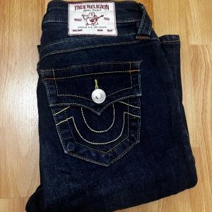True Religion mörkblå jeans med kontrastsömmar - Mörkblå jeans från True Religion med ikoniska kontrastsömmar och stora bakfickor med lock och silverfärgade knappar. Klassisk passform och snygg detaljrik design, perfekt för dig som vill sticka ut med dina jeans. aldrig använt helt nya. köpta från nelly. modellen becca 