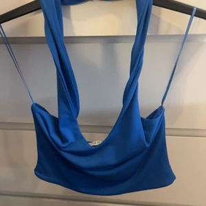 Blå axelväska i mjukt tyg - Säljer en snygg blå axelväska med draperad design och bred axelrem. Väskan är tillverkad i ett mjukt tygmaterial och har en modern, avslappnad look. Perfekt för dig som vill ha en unik och trendig accessoar till din outfit.