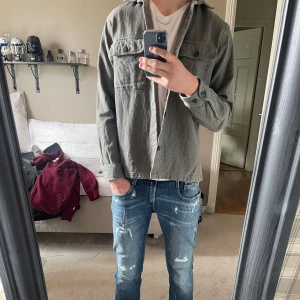 Grå grön overshirt från Jack & Jones - Säljer en stilren grå overshirt från Jack & Jones. Jackan har två bröstfickor med knappar, klassisk krage och är tillverkad i ett mjukt bomullsmaterial. Perfekt att slänga över en t-shirt för en avslappnad look. I väldigt bra skick, möjligtvis lite uttröttad men inga sakliga fel. Hör av dig om du undrar över något, pris går att diskutera
