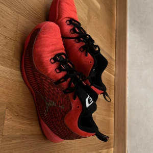 Röda Jordan sneakers med svart detalj - Säljer ett par röda Jordan sneakers med svart plös och svarta skosnören. Skorna har det klassiska Jumpman-loggan på sidan och en cool mönstrad detalj i rött och silver. Ovandelen är i textil och syntet, perfekt för dig som gillar sportig stil.