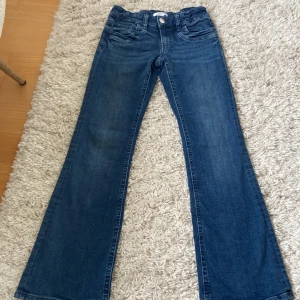 Blå bootcut jeans från Gina Tricot - Snygga blå jeans från Gina Tricot i klassisk bootcut-modell. Jeansen har fem fickor, knapp och dragkedja framtill. Perfekta för dig som gillar en lite utsvängd stil och vill ha ett par bekväma jeans i bomull.