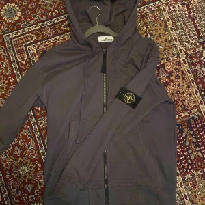 Mörkgrå hoodie från Stone Island - Kan gå ner oanvänt Säljer en mörkgrå hoodie från Stone Island med klassisk patch på ärmen. Tröjan har huva, dragkedja framtill och två fickor. Perfekt för dig som gillar streetwear och vill ha något stilrent med edge. Storlek L, riktigt snygg och bekväm.