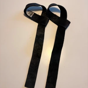 Svarta lyftremmar från Better Bodies - Säljer ett par svarta lyftremmar från Better Bodies i äkta skinn. Remmarna är breda och slitstarka, perfekta för gymmet och tunga lyft. De har en klassisk design med förstärkta sömmar och mjuk insida för extra komfort.
